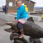 Isla Brown, age 5, sits on Wildheart, the Giving Salmon, sculpture Saturday, May 12, 2018 at the ribbon cutting for the Homer Boat House. (Photo by Michael Armstrong/Homer News)