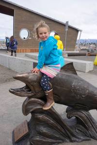Isla Brown, age 5, sits on Wildheart, the Giving Salmon, sculpture Saturday, May 12, 2018 at the ribbon cutting for the Homer Boat House. (Photo by Michael Armstrong/Homer News)