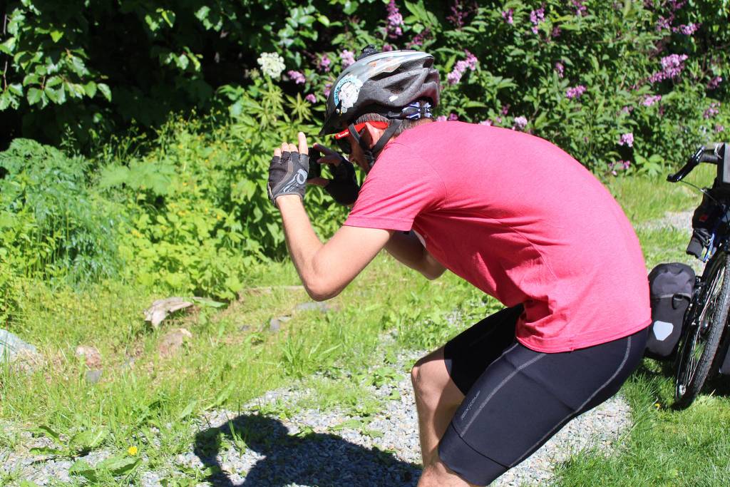 Chris Haag bends down to take a photo of his bike, packed with about 100 pounds of gear and food for a trek from Alaska to Argentina, as it leans up against the side of an old wooden building on Monday, July 2, 2018 in Homer, Alaska. Haag, who set off on Monday for the two-year journey with his wife, said its a sort of long-distance cycling tradition to take a picture of ones bike in front of old or reclaimed wood. (Photo by Megan Pacer/Homer News)