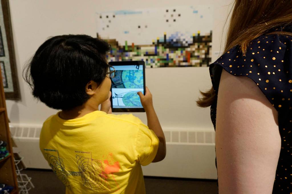 Chloe Adkison views an image in an iPad from the Dirigibles of Denali show at the Pratt Museum at the July 6, 2018 First Friday opening in Homer, Alaska. The images appear when viewed through the HP Reveal augmented reality app. (Photo by Michael Armstrong/Homer News)
