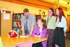 Nikolaevsk senior Megan Hickman, at table, signs a contract to commit to play basketball for the University of Alaska Fairbanks this fall. Her father Bobby Hickman, left, mother Kelli Hickman, second from right, and sister Isabelle Hickman, far right, joined Megan in the Nikolaevsk library on April 13 for the signing.-Photo provided