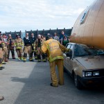 Nationally recognized firefighting extraction teacher Ron Moore of Plano, Texas, explains different ways to save victims in an automobile crushed by an overturned object. He identifies the challenges of weak points in the vehicle and the different approaches to saving lives. For the learning exercise, firefighters used a forklift and front-end loader to roll the school bus, an expired bus donated by First Student of Homer, onto a Subaru.-Photo by Heather Ericson
