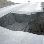 Two people stand at the top of the hill above the road collapse on Kachemak Drive.-Photo by Michael Armstrong, Homer News