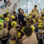 Members of the Kachemak Swim Club gather around the club’s Head Coach, Neil Romney, for a team cheer Saturday morning, the second day of the 2015 End of the Road meet at the Kate Kuhns Aquatic Center.-Photo by McKibben Jackinsky, Homer News