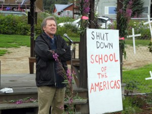 Father Roy Bourgeois speaks last Saturday afternoon at WKFL Park. The fence with crosses in the right of the photo duplicates protests done at the gates of U.S. Army base Fort Benning, Ga.-Photo by Michael Armstrong, Homer News