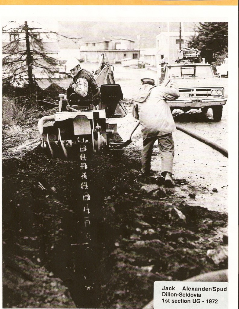 HEA crew puts in underground power lines in 1972 in Seldovia.  Jack Alexander is on the equipment and Spud Dillon works with the shovel.-Photo courtesy of HEA
