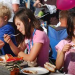 Audrey Dabney, center, and Keeley Dabney, right, eat at the Governor’s Family Picnic last Thursday.-Photo by Michael Armstrong, Homer News