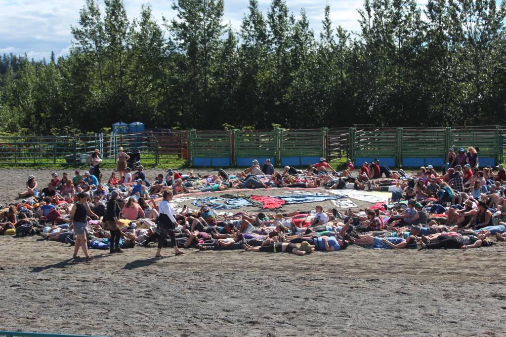 Volunteers and festival goers take their places on the ground to be part of this years art installation at Salmonfest on Saturday, Aug. 4, 2018 in Ninilchik, Alaska. Coordinated each year by Homer artist Mavis Muller, the project is a human and fabric mosaic piece which always includes a message about the importance of salmon and water. The installation is completed by being photographed from above by a drone. (Photo by Megan Pacer/Homer News)