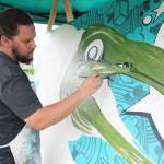 Colorado artist Patrick Maxcy works on a painting of a salmon during a public barbecue at Karen Hornaday Park for Alaska Wild Salmon Day on Friday, Aug. 10, 2018 in Homer, Alaska. Cook Inletkeeper has partnered with The Bunnell Street Arts Center to host Maxcy as artist in residence for August. (Photo by Megan Pacer/Homer News)