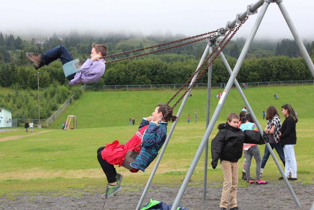 Daniel Kulikov, left, and Addie Moore, center, swing while Aiden Clark, right, stands near the swings during recess Tuesday, Aug. 18, 2018 on the first day of school at West Homer Elementary in Homer, Alaska. (Photo by Megan Pacer/Homer News)