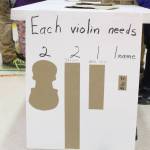 A sign advises students and parents how to make cardboard violins during a craft night at Paul Bank Elementary School on Thursday, Sept. 6, 2018 at the school in Homer, Alaska. The project is part of the schools Preludes Violin Program, which teaches first and second grade students musicianship and the host of skills that come with it. Students start out with the cardboard violins before graduating to the real instruments later in the year. (Photo by Megan Pacer/Homer News)