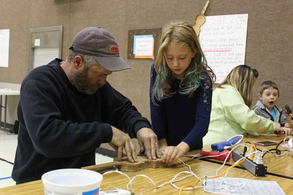 Reilly Sue Baker, 9, makes a violin out of cardboard with the help of her dad, Bryan Baker, on Thursday, Sept. 6, 2018 at Paul Banks Elementary School in Homer, Alaska. The violin-making project is part of the schools Preludes Violin Program, which puts real violins in the hands of elementary students after months of learning learning the necessary skills to handle one. The music instruction is used to enhance their learning experience. (Photo by Megan Pacer/Homer News)