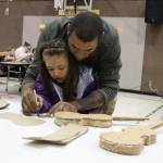 Alonzo Lang helps his 5-year-old daughter, Payton, create a violin out of cardboard during a craft night at Paul Bank Elementary School on Thursday, Sept. 6, 2018 at the school in Homer, Alaska. The project is part of the schools Preludes Violin Program, which teaches first and second grade students musicianship and the host of skills that come with it. Students start out with the cardboard violins before graduating to the real instruments later in the year. (Photo by Megan Pacer/Homer News)