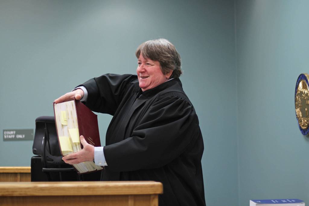 Homer District Court Judge Margaret Murphy holds up one of several volumes of laws to show a groups of Fireweed Academy students during their Oct. 8, 2018 field trip to the Homer Courthouse in Homer, Alaska. She showed them the book in response to a students question of: How many law are there? (Photo by Megan Pacer/Homer News)