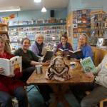 The staff and partners in the Homer Bookstore pose for a photo in the stores cafe in Homer, Alaska, on Oct. 29, 2018. From left to right are Sue Post, partner; Jennifer Norton, staff; Jennifer Stroyeck, partner; Nancy Vait, staff; Sara Reinert, staff; and Lee Post, partner. The sculpture on the table is of bookstore matriarch Joy Post, mother of Sue and Lee Post, and was sculpted by artist Barbara Jo Auburn House. (Photo by Michael Armstrong/Homer News)
