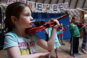 First grade student Elizabeth Parke practices holding a cardboard violin, in anticipation of the real thing, at Fireweed Academy in Homer, Alaska. (Photo by Miranda Weiss)