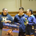 Luciano Fasulo holds a banner recognizing him at Senior Night, the Homer-Kenai dual wrestling meet held Nov. 21, 2018, in the Homer High School Alice Witte Gym, Homer, Alaska. Supporting hi are Greg and Janie Martin. (Photo by Michael Armstrong/Homer News)