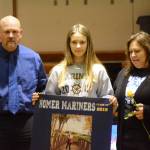 Allison Wells holds a banner recognizing her at Senior Night, the Homer-Kenai dual wrestling meet held Nov. 21, 2018, in the Homer High School Alice Witte Gym, Homer, Alaska. Supporting her are her parents, Bubba and Mike Wells.(Photo by Michael Armstrong/Homer News)