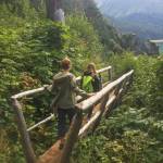Two hikers cross a wooden bridge while making their way down the Saddle Trail on Friday, Aug, 17, 2018 in Kachemak Bay State Park across Kachemak Bay from Homer, Alaska. While some trails are still impassable, there are many routes — like Glacier Lake to Saddle — with clear, dry trails. (Photo by Megan Pacer/Homer News)