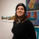 Sarah Frary stands by her paintings, Anatomical Landscape, left, at the First Friday, Dec 7, 2018, opening of Bunnell Street Arts Centers 10x10 show in Homer, Alaska. (Photo by Michael Armstrong/ Homer News)