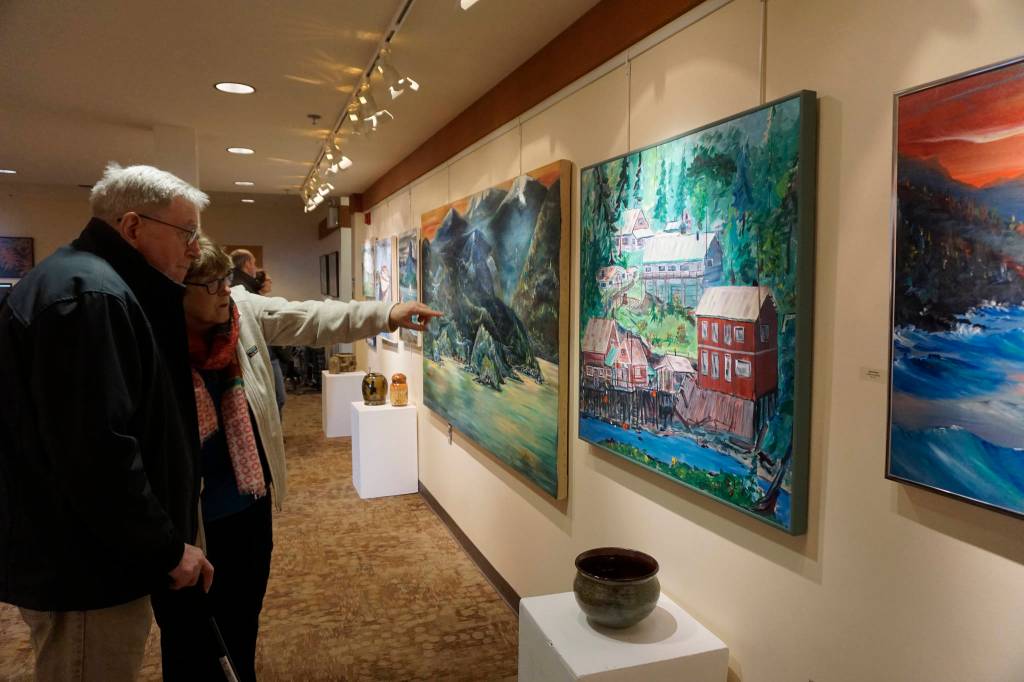 Franco and Caroline Venuti look at John Fenskes paintings at the First Friday, April 5, 2019, opening for his retrospective showing at Kachemak Bay Campus in Homer, Alaska. (Photo by Michael Armstrong/Homer News)