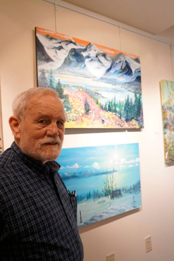 Bill Smith stands by a John Fenske painting, top, that his children bought for him. Fenskes retrospective show opened on First Friday, April 5, 2019, at Kachemak Bay Campus in Homer, Alaska. (Photo by Michael Armstrong/Homer News)