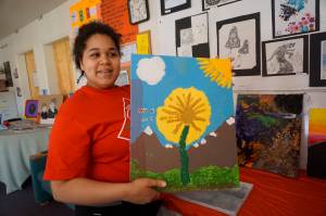 Flex School student Makayla Prescott holds up a collage she showed at Flex First Friday, an exhibit of art done by Flex students, teachers and staff over the past year. The show included pottery created during an Artist in the School residency by Jeff Szarzi. (Photo by Michael Armstrong/Homer News)
