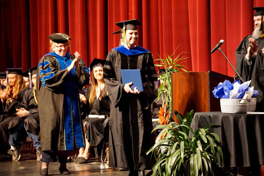 Emilie Springer smiles after receiving her doctor in anthropology degree and hood at the Kachemak Bay Campus commencement last Wednesday, May 8, 2019, at the Mariner Theatre in Homer, Alaska. Applauding at left is KBC interim campus director Paula Martin. A Homer resident from Ninilchik, Springer received her doctorate from the University of Alaska Fairbanks but chose to receive her PhD. in her home town  the first doctorate to do so at KBC commencement. (Photo by Michael Armstrong/Homer News.)
