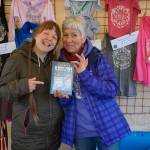 Homer Farmers Market Director Robbi Mixon, left, and Margarida Kondak, right, display of copy of the Homer Farmers Market Cookbook at the opening of the market on May 25, 2019, in Homer, Alaska. (Photo by Michael Armstrong/Homer News)