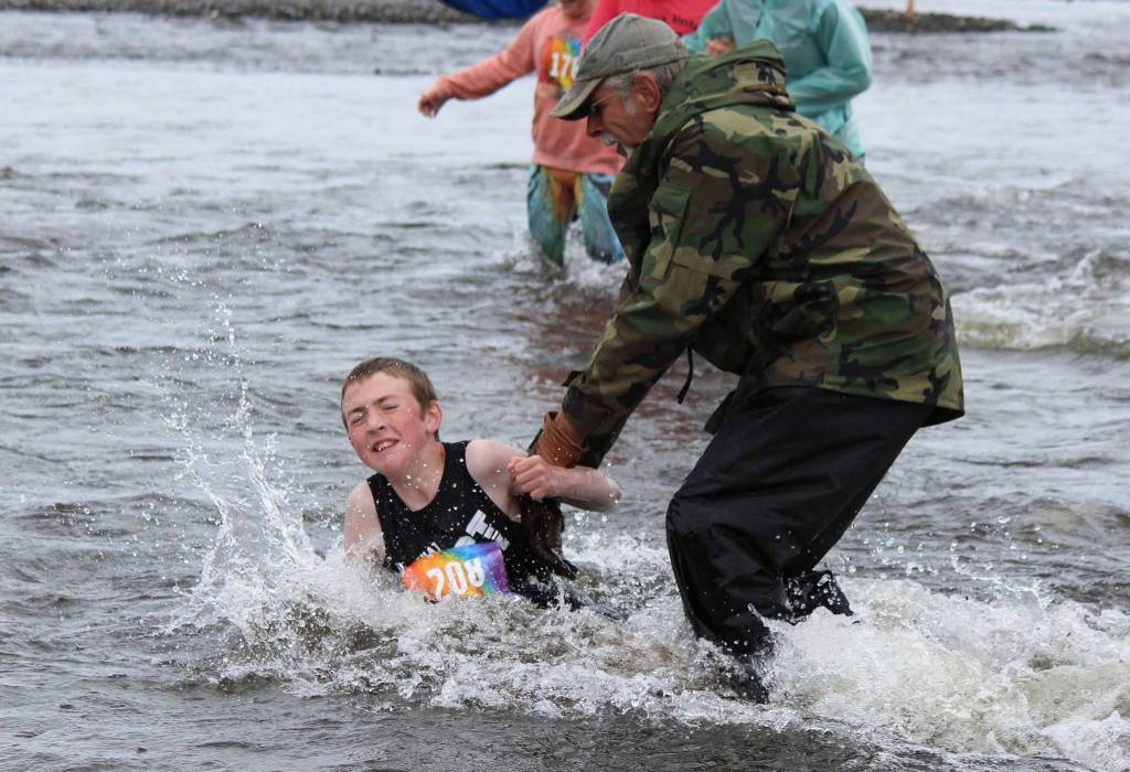 A cold-water stumble doesnt slow runner Kael Aamodt, 111, thanks to a little help from a race volunteer during the Clam Scramble held Saturday, June 15, 2019 in Ninilchik, Alaska. (Photo by McKibben Jackinsky)