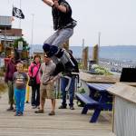 Jabali Trippsmith jumps on bouncing stilts as the New Old Time Chautauqua Fighting Instruments of Karma Marching Chamber Band Orchestra performs in the Homer Boathouse at the Homer Harbor on July 2, 2019, in Homer, Alaska. (Photo by Michael Armstrong/Homer News)