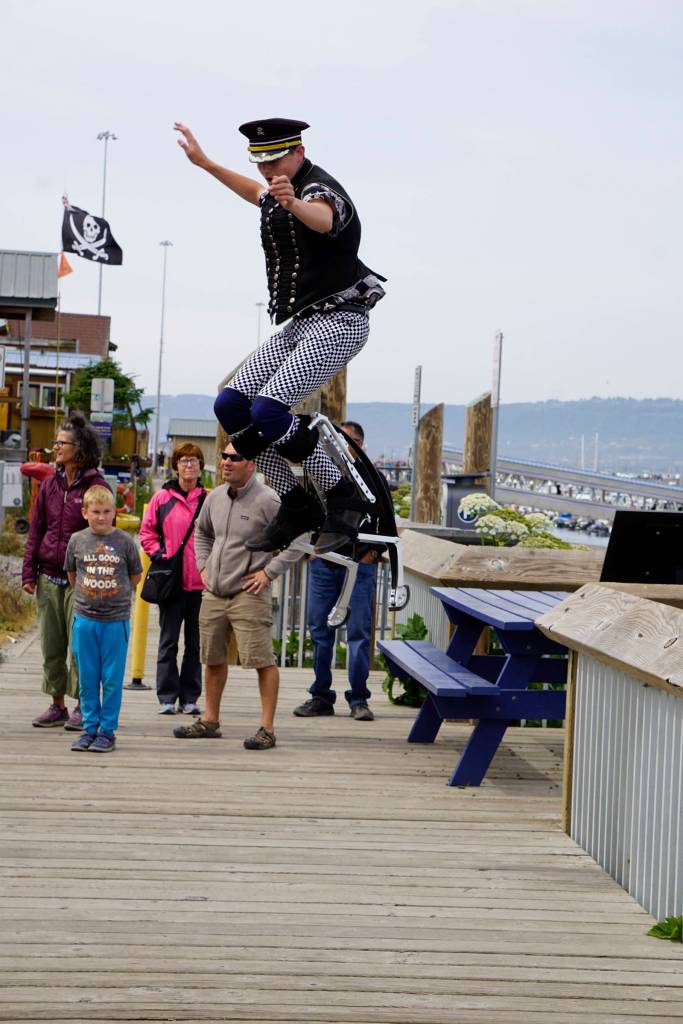 Jabali Trippsmith jumps on bouncing stilts as the New Old Time Chautauqua Fighting Instruments of Karma Marching Chamber Band Orchestra performs in the Homer Boathouse at the Homer Harbor on July 2, 2019, in Homer, Alaska. (Photo by Michael Armstrong/Homer News)