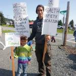 Nako Cook, left and Jared Cook, right, hold signs at a rally Sunday, July 28, 2019, against Gov. Mike Dunleavys budget cuts at the Legislative Information Office, Homer, Alaska. (Photo by Michael Armstrong/Homer News).