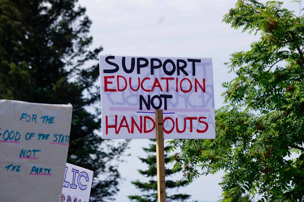 A demonstrator holds a sign at a rally Sunday, July 28, 2019, against Gov. Mike Dunleavys budget cuts at the Legislative Information Office, Homer, Alaska. (Photo by Michael Armstrong/Homer News).