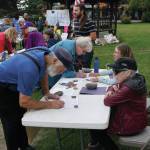 Recall Dunleavy organizers Ann Keffer, right, in hat, and Pat Cue, behind Keffer, take signatures at a Recall Dunleavy rally held on Aug. 1, 2019, at WKFL Park in Homer, Alaska. At left, former Homer Rep. Paul Seaton, NP-Homer, signs a form. Seaton lost to Rep. Sarah Vance, R-Homer, in the general election. (Photo by Michael Armstrong)