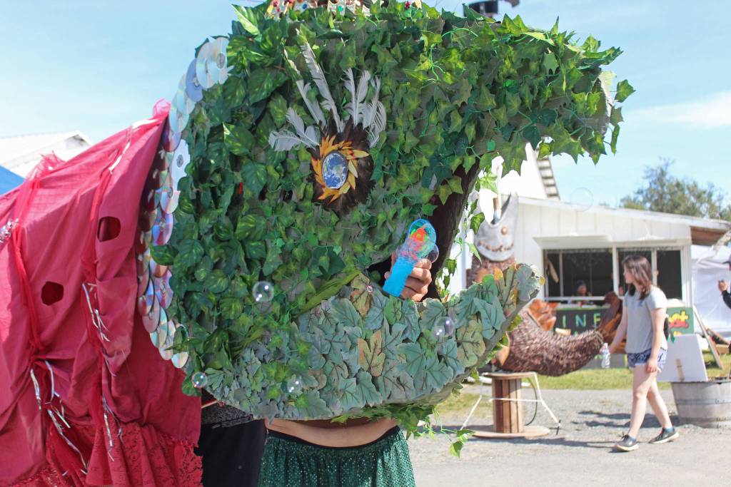 A volunteer heading up the group powering Queen Marie the giant salmon uses a bubbler blower to blow bubbles out of the large puppets mouth while volunteers march her around Salmonfest on Saturday, Aug. 3, 2019 in Ninilchik, Alaska. (Photo by Megan Pacer/Homer News)
