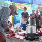 Passersby watch as Jeff Lockwood, host of the KBBI cooking talkshow Check the Pantry prepares a salmon during a food demonstration Saturday, Aug. 3, 2019 at Salmonfest in Ninilchik, Alaska. (Photo by Megan Pacer/Homer News)