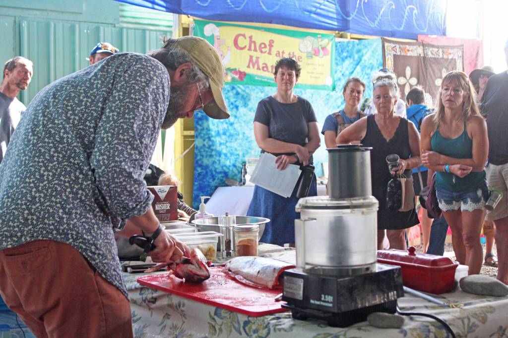 Passersby watch as Jeff Lockwood, host of the KBBI cooking talkshow Check the Pantry prepares a salmon during a food demonstration Saturday, Aug. 3, 2019 at Salmonfest in Ninilchik, Alaska. (Photo by Megan Pacer/Homer News)
