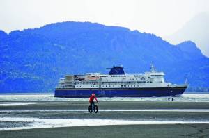 A man rides a fat bike on the Homer Spit beach as the M/V Kennicott leaves on Sept. 1, 2019, out of Homer, Alaska. (Photo by Michael Armstrong/Homer New)