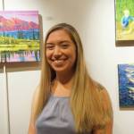 Maria Bernier poses by some of her paintings at her show at Kachemak Bay Campus that opened on First Friday, Oct. 4, 2019, in Homer, Alaska. (Photo by Michael Armstrong/Homer News)
