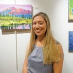 Maria Bernier poses by some of her paintings at her show at Kachemak Bay Campus that opened on First Friday, Oct. 4, 2019, in Homer, Alaska. (Photo by Michael Armstrong/Homer News)
