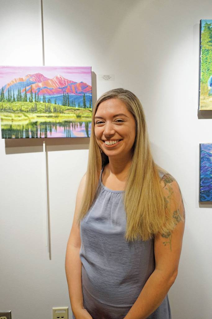 Maria Bernier poses by some of her paintings at her show at Kachemak Bay Campus that opened on First Friday, Oct. 4, 2019, in Homer, Alaska. (Photo by Michael Armstrong/Homer News)