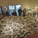 First Friday visitors hold up Amber Webbs kuspuk at the opening of the Kuspuk/Qaspeq/Atikluk show on Oct. 5, 2019, at Bunnell Street Arts Center in Homer, Alaska. The kuspuk shows faces of missing or murdered indigenous women. (Photo by Michael Armstrong/Homer News)