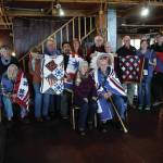 Veterans who received Quilts of Valor pose for a photograph at the Veterans Day lunch held at the Elks Lodge on Nov. 11, 2019, in Homer, Alaska. The quilts were made by the Kachemak Bay Quilters and presented as part of the national Quilts of Valor project. Since being founded by Catherine Roberts in 2003 while her son was deployed in Iraq, the program has given more than 235,000 quilts to military veterans, with almost 2,000 awarded in Alaska. Veterans who received quilts are, seated at left, John Benya; fifth from left, Troy Wise; sixth from left, Robert R.J. Carlough; eighth from left, Norman Mosher; ninth from left, in chair, Thomas Youngblood; fourth from right, Robert Fimon; and second from right, Nicholas Varney. (Photo by Michael Armstrong/Homer News)