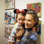 Carla Klinker Cope and her daughter, Nova, pose next to their paintings at left at the Nov, 8, 2019, opening of the 10x10 show at Bunnell Street Arts Center. Nova painted the background elements to the paintings and her mother added to that. (Photo by Michael Armstrong/Homer News)