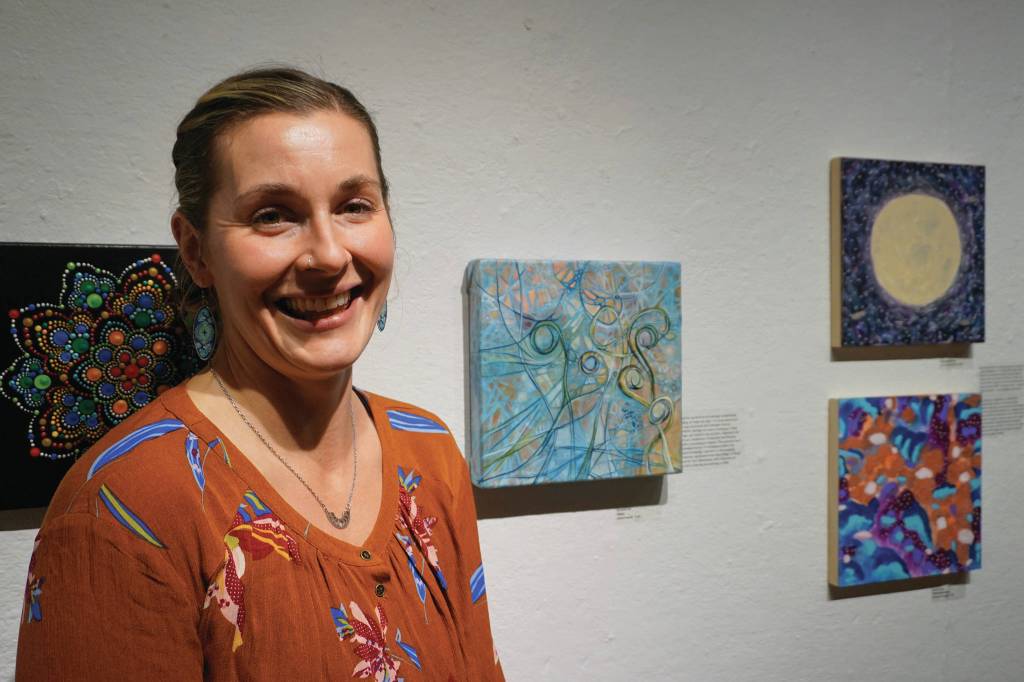 Brianna Lee stands by her painting, Cipher, one of the works of art in the 10x10 show at Bunnell Street Arts Center that opened on Nov. 8, 2019, in Homer, Alaska. (Photo by Michael Armstrong/Homer News)