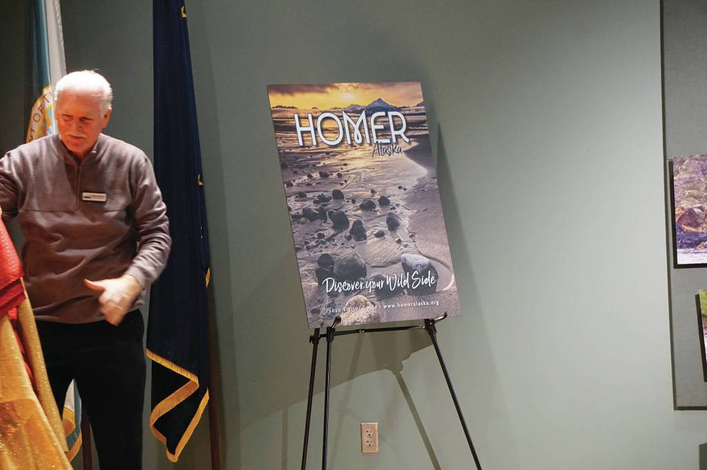 Homer Chamber of Commerce and Visitor Center Executive Director Brad Anderson unveils the cover of the 2020 Visitor Guide at the chambers annual meeting on Jan. 21, 2020, at the Alaska Islands and Ocean Visitor Center in Homer, Alaska. Edward L. Marsh took the photo on the cover. (Photo by Michael Armstrong/Homer News)