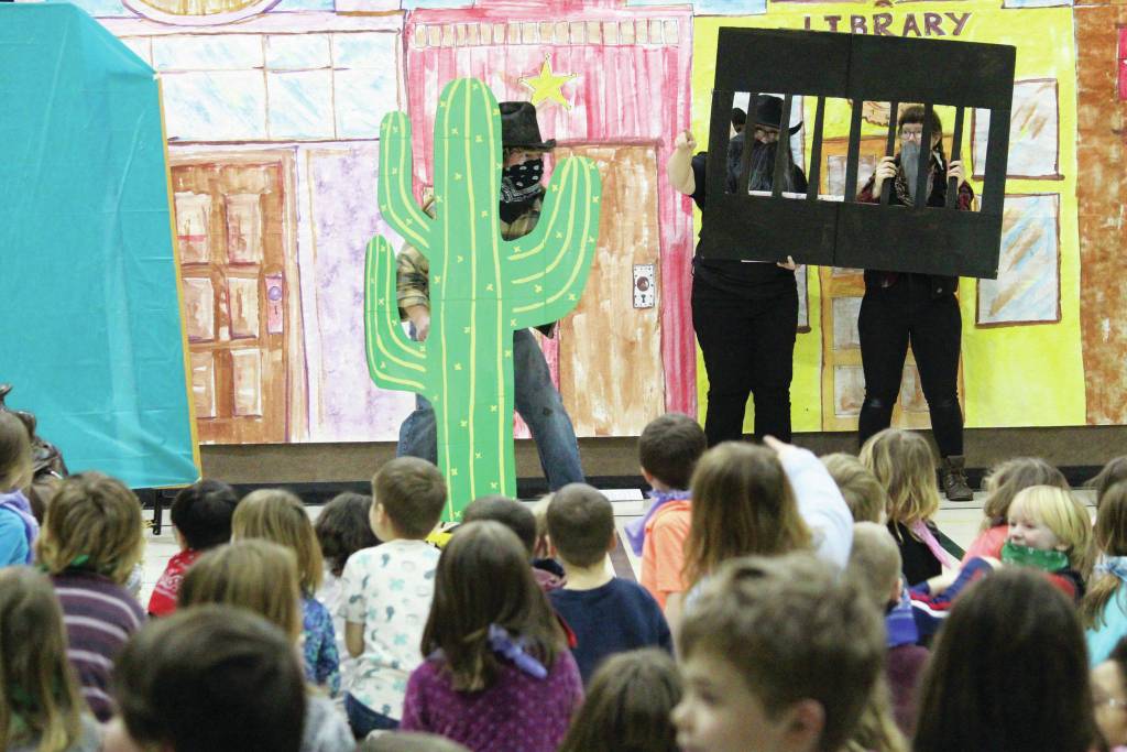 Paul Banks Elementary School staff member Jake Parrett hides behind a makeshift cactus whilst pretending to be a bandit during an assembly celebrating the start of the schools annual read-a-thon on Feb. 3, 2020 at the school in Homer, Alaska. To his right are Jeri McLean and Maria Fourier. (Photo by Megan Pacer/Homer News)