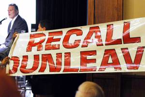 Bill Roth | Anchorage Daily News                                Protesters unfurl a banner as Gov. Mike Dunleavy speaks during a roadshow with Americans for Prosperity in 49th State Brewing Company in Anchorage on March 26.