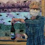 Grace Ridge Brewery co-owner Sherry Stead holds up a bottle of special Kachemak Bay State Park 50th anniversary honey pale ale on Saturday, May 16, 2020, at the brewery in Homer, Alaska. Homer artist Kathy Sarns designed the label. (Photo by Michael Armstrong/Homer News)
